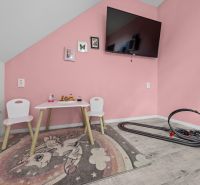 A children's room in a family house with pink walls, a table, and a TV on the wall.