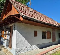 A family house in Mikušovce with wooden shutters and a red roof surrounded by greenery.