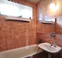 A family house bathroom with a bathtub, a sink, and tiled walls in a brown shade.