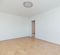 An empty room with wooden floor decor and a view into the kitchen in a 3-room apartment.