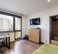 A room in a 4-room apartment with a wooden decor floor, a desk, and a television.