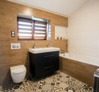 A bathroom in a family house with a bathtub, a sink, and a floor with a wooden decor.