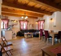 The living room of a family house with wooden ceilings, a floor with a wood pattern, and red curtains.