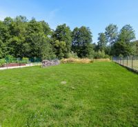 The garden of a family house in Očová with a lawn and fencing, surrounded by forest.