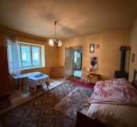 The interior of a family house with a bed, table, and wood stove, styled in warm tones.