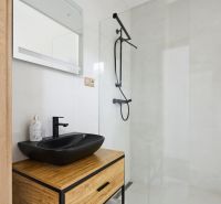 A bathroom in a 3-room apartment with a black sink, shower, and wooden decor.