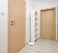 In the hallway of the 2-room apartment, there is a white shelf and a coat rack on light-colored tiles.