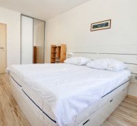 A bedroom with a wood-patterned floor, a large bed, and a built-in wardrobe in a 2-room apartment.