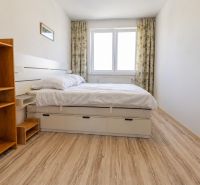 A bedroom in a two-room apartment with a bed, a shelving unit, and a floor with a wood decor.
