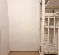 Storage space with white shelves in a 2-room apartment, with carpeted flooring.