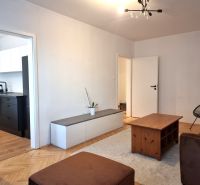 Living room in a two-room apartment with a wooden decor floor, visible into the kitchen.