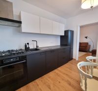 A kitchen in a 2-room apartment with black appliances and a wooden decor floor.