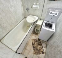 A bathroom in a 3-room apartment with a bathtub, washing machine, and tiles.