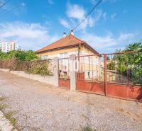 A family house in Nitra with a fence and a sloped roof, with a block of flats in the background.