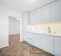 A kitchen in a 3-room apartment with white furniture and a wooden decor floor.
