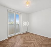 An empty room with a wooden decor floor and balcony doors in a 3-room apartment.