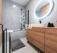 A bathroom with wooden decor in a family house, featuring a bathtub and an oval mirror with lighting.