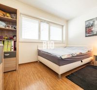 A bedroom in a family house with a wooden decor floor and a shelf full of books and toys.