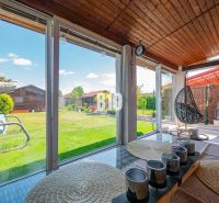 A glazed terrace of a family house in Nitra with a view of the garden and wooden decor.