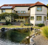 A family house in Podersdorf am See with a large garden, a pond, and solar panels.