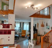 Interior of a family house with a ceramic fireplace, plants, and wooden stairs.