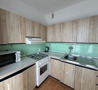 A kitchen in a 3-room apartment with a wooden decor floor and wooden cabinets.