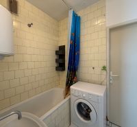 A bathroom in a 3-room apartment with a bathtub, a washing machine, and white tiles.