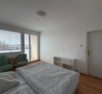 A bedroom in a 3-room apartment with a wood-patterned floor, a bed, and chairs.