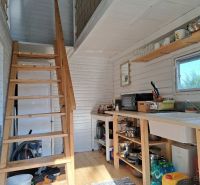 Interior of a cabin with a staircase, kitchen, and wooden decor flooring.
