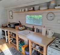 A kitchen in a cottage with shelves, a counter, and a floor with a wood decor.