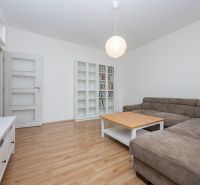 Living room in a three-room apartment with a wooden decor floor, a sofa, and a bookshelf.