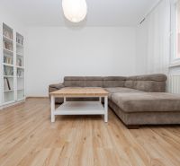 Living room with a comfortable sofa, a bookshelf, and a wooden-patterned floor in a three-room apartment.