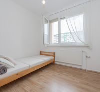 A single bed and a window with white curtains in a 3-room apartment on a floor with a wooden decor.