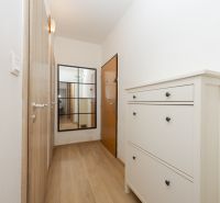 Narrow hallway with wood-patterned flooring, a mirror, and a white shoe cabinet.