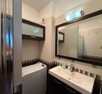 A bathroom with a sink, mirror, shower, and washing machine in a 3-room apartment.