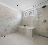 A bathroom in a family house with a bathtub and a shower, tiled with light tiles.