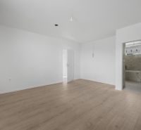 A nondescript room in a family house with a wood-patterned floor and white walls.