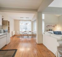 A recreational apartment with a wooden decor floor, kitchen, dining table, and comfortable seating.