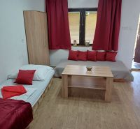 Interior photograph of a cabin with a bed, table, and red accessories.