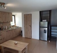 Interior of a cabin with a kitchen unit, refrigerator, and staircase, floor with wooden decor.