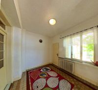 In the family house, there is a room with a colorful carpet, a window, and a wall with a radiator.