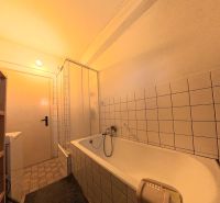 Bathroom with a bathtub, shower, and tiles in a family house.
