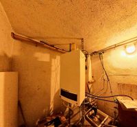 Bathroom in a family house with fixtures and pipes, illuminated by a light bulb.