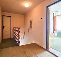 A hallway in a family house with wooden railings, open doors, and carpeted flooring.