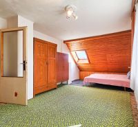 A room in a family house with wooden elements, a bed, and a green carpet.