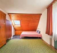 Attic bedroom in a family house with a wooden wall and patterned carpet.