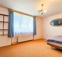 A room in a family house with a window, shelves, and a bed, carpeted floor.