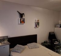 Studio apartment with a bed, wall decorations, and a chair next to the refrigerator.