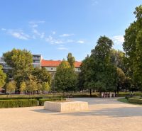 A garden with colorful flowers, trees, and buildings in Bratislava - Old Town on Banskobystrická.