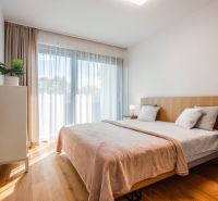 Bedroom in a two-room apartment with a bed, curtains, nightstands, and a floor with a wood decor.